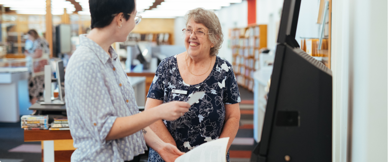 Two women talking at the borrow counter at the library