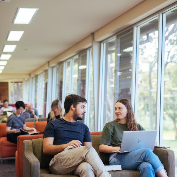 Man & woman sitting on lounge talking in library